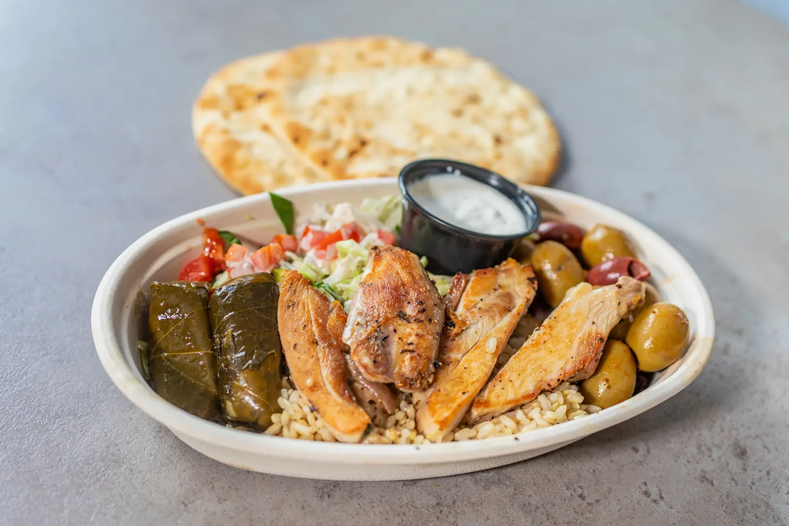 A complete Skull Creek Greek classic plate with chicken, rice, salad, pita and sides